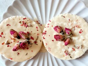 Two elegant rose-infused white chocolate discs on a textured white plate.