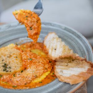 A mouth-watering plate of ravioli with rich tomato sauce, garnished with parmesan and served with crispy bread.